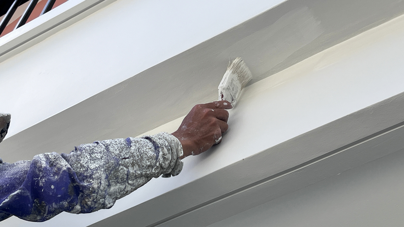 A worker is painting the walls of the house with a primer using a paint brush.