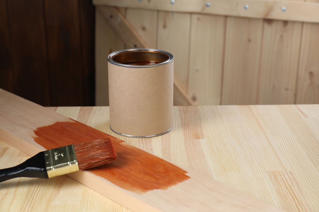 Can and brush with wood stain on wooden surface, space for text